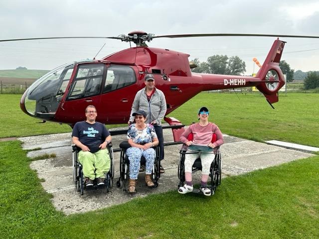 Gruppe von Rollstuhlfahrern vor dem Helikopter. Alle freuen sich nach diesem Flugerlebnis